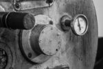 A detailed black and white image of an industrial coffee roaster machine, highlighting gauge and metal textures.