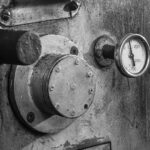 A detailed black and white image of an industrial coffee roaster machine, highlighting gauge and metal textures.