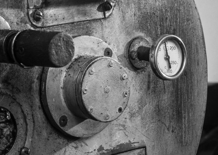 A detailed black and white image of an industrial coffee roaster machine, highlighting gauge and metal textures.